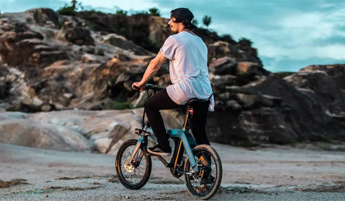 A cyclist on the Fiido D11 ebike exploring a rocky coastal terrain at sunset.