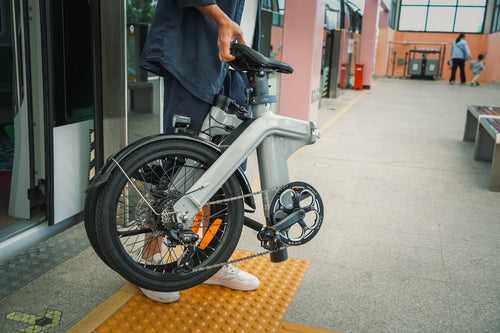 A man is carrying a folded Fiido D11 mini electric bike.