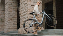 A woman effortlessly lifts a Fiido Air lightweight electric bike up the stairs.