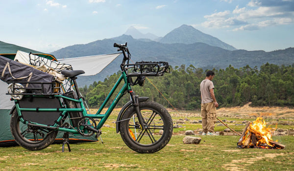 Fiido T2 electric cargo bike loaded with camping gear at a mountain campsite beside a tent and campfire.