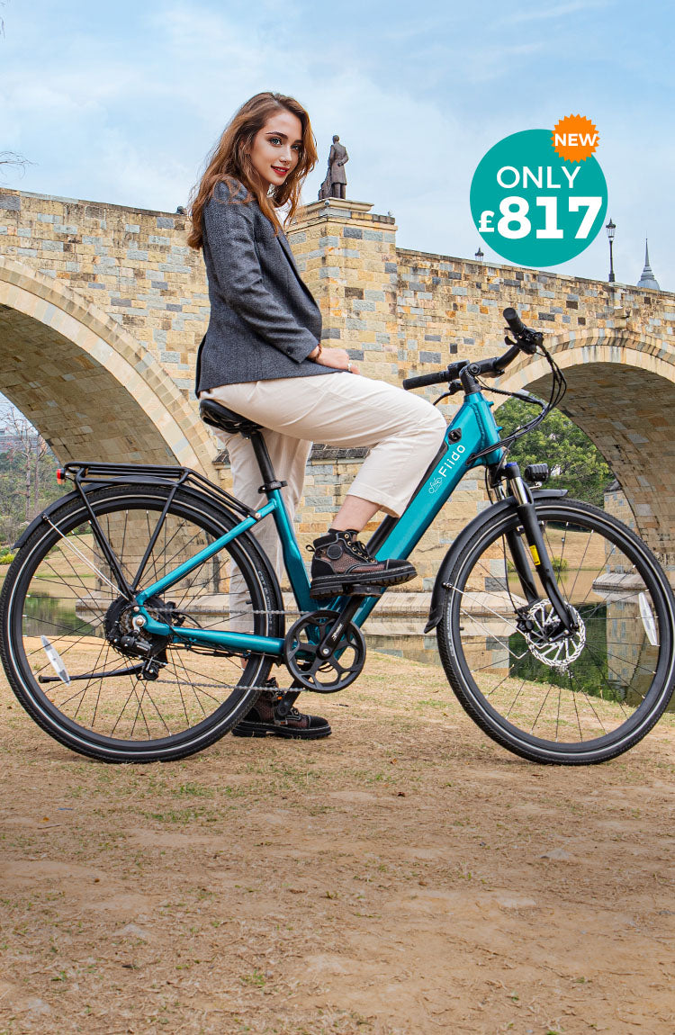 A woman rides a Fiido C11 electric bike by the river under a bridge.